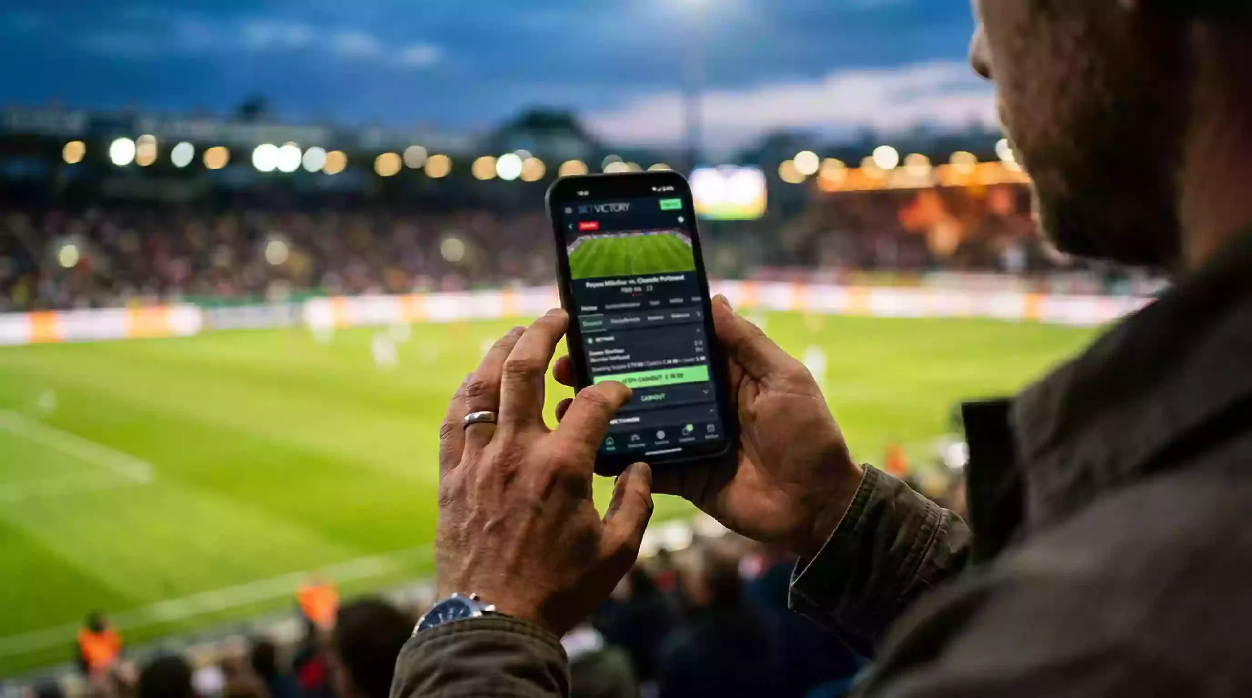 Cash-Out bei Sportwetten – Hand hält Smartphone mit Fußballspiel im Hintergrund